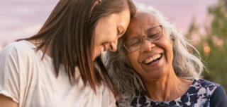 Mother with white hair and daughter with brown hair lovingly touching heads, laughing